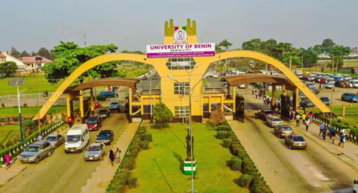 A vibrant entrance gate to the University of Benin, featuring a large yellow arch with a sign on top. Vehicles and people move below, surrounded by greenery.
