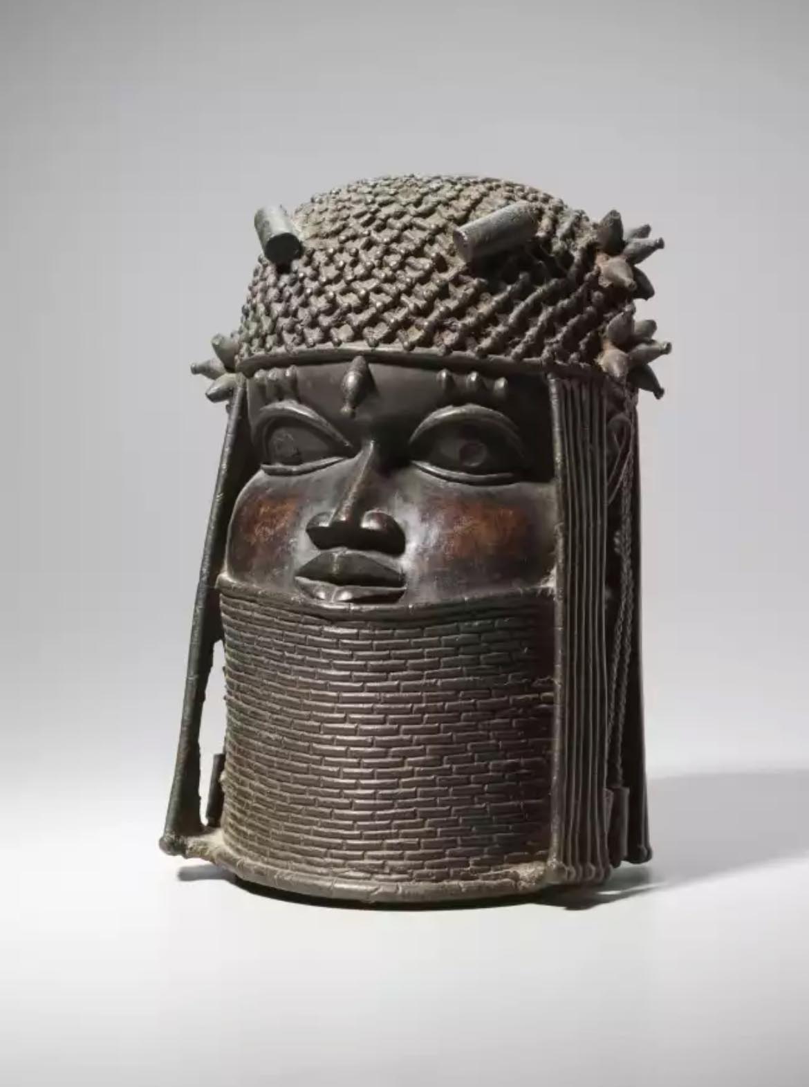Alt Text: Bronze head sculpture with intricate braided hair, ornate patterns, and a serene expression. The detailed headdress conveys cultural richness.